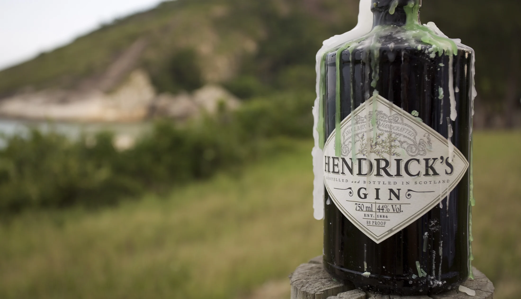 Garrafa Hendrick’s Gin em destaque, com a paisagem da praia ao fundo.