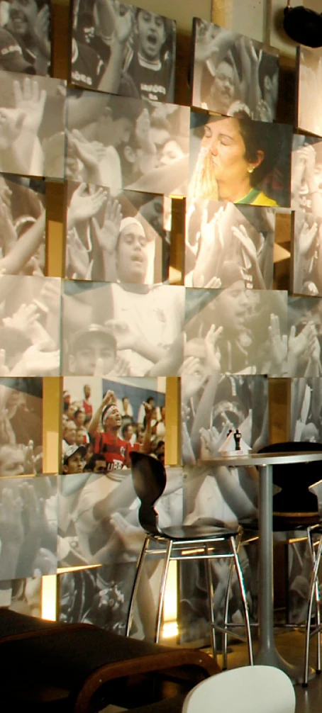 Painel de fotografias de torcedores e bancos altos junto à parede do bar.